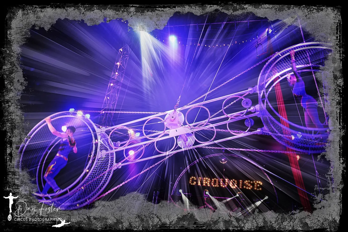 Two performers inside the rings of a rotating double wheel high in the big top, with the Cirquoise sign lit up below