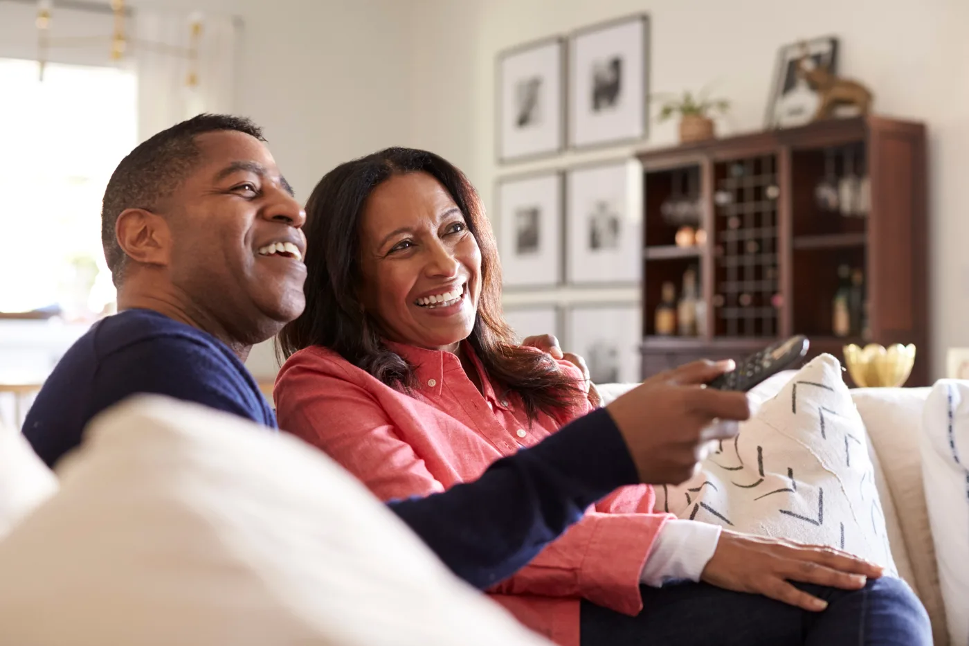 Two people laughing on a sofa while watching television at home