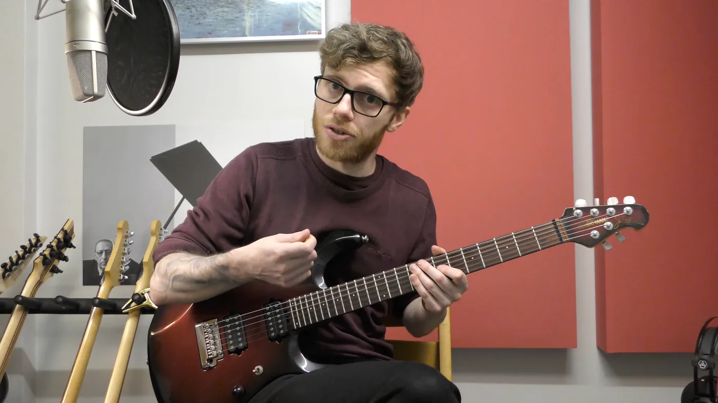 An electric guitar in the home studio, with a microphone and a rack of guitars alongside.